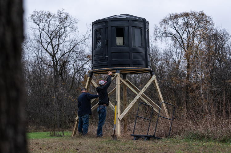A deer hunting blind with a ladder, suitable for hunting, showcasing RAM 650 acrylic windows for both bow and gun enthusiasts.
