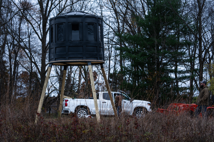 A deer hunting blind with a ladder, suitable for hunting, showcasing RAM 650 acrylic windows for both bow and gun enthusiasts.